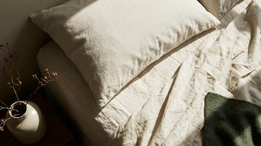 Almohada con funda clara sobre sábanas de lino hueso con la luz de la mañana entrando de lado